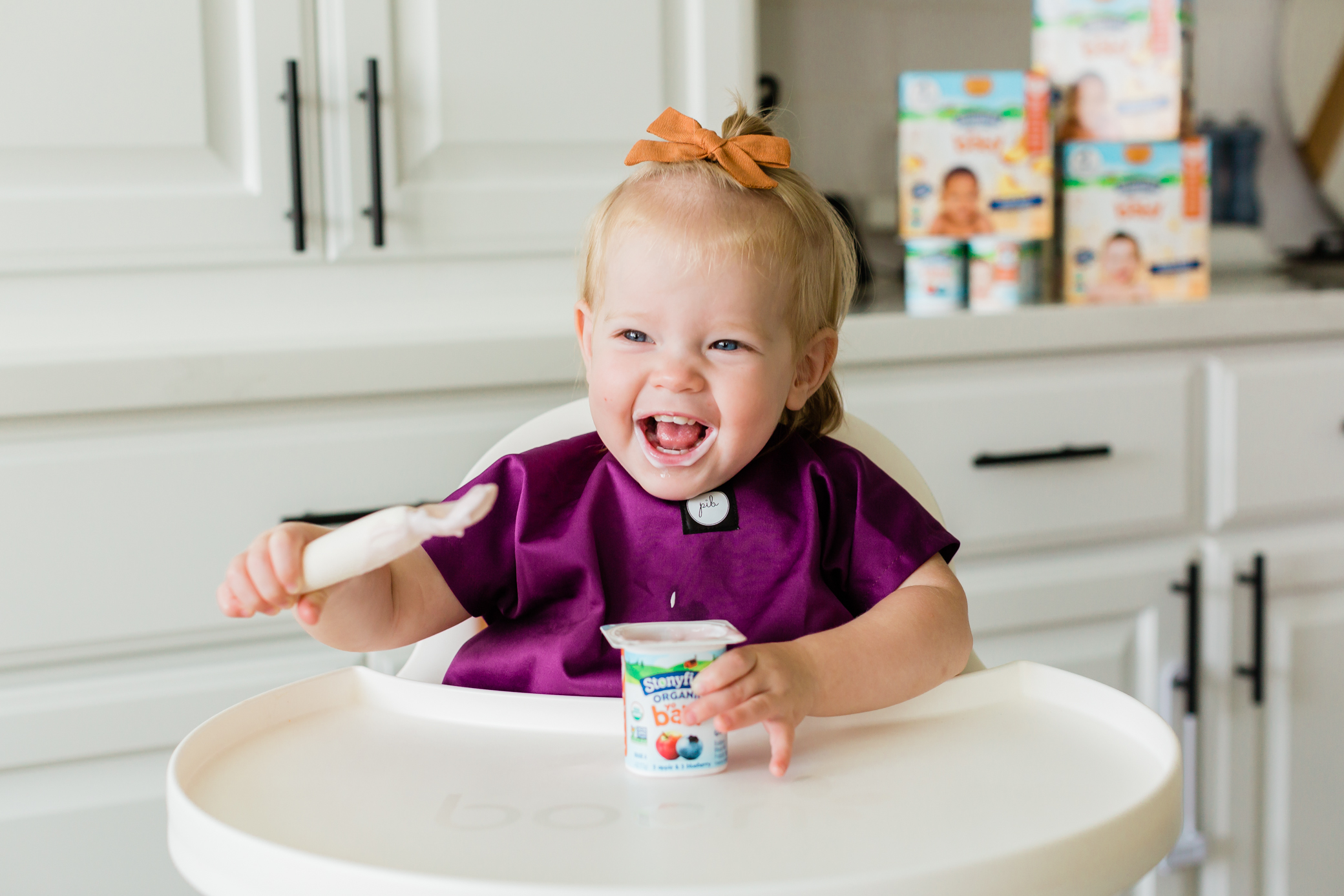 Cô bé đang ngồi trên ghế cao ăn sữa chua Stonyfield.
