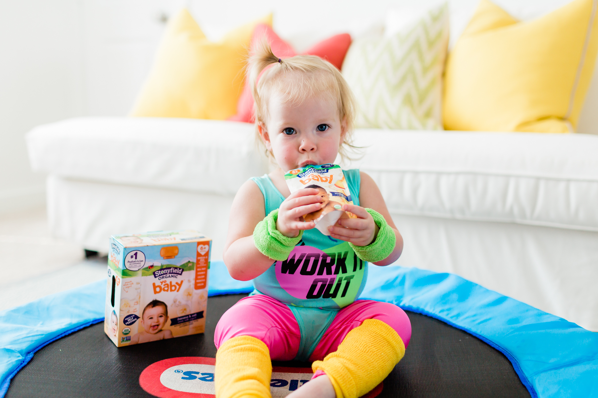 Cô gái trẻ đang ngồi trên tấm bạt lò xo của mình và ăn một túi sữa chua stonyfield.