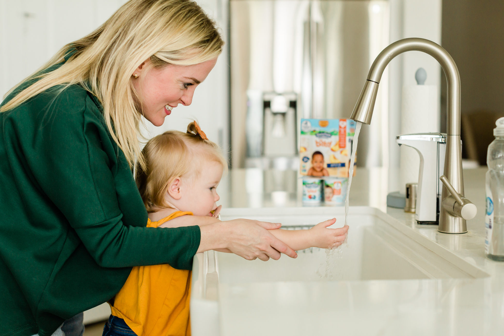 Những người mẹ đứng sau cô con gái nhỏ khi giúp cô rửa tay ở bồn rửa tay trong bếp.